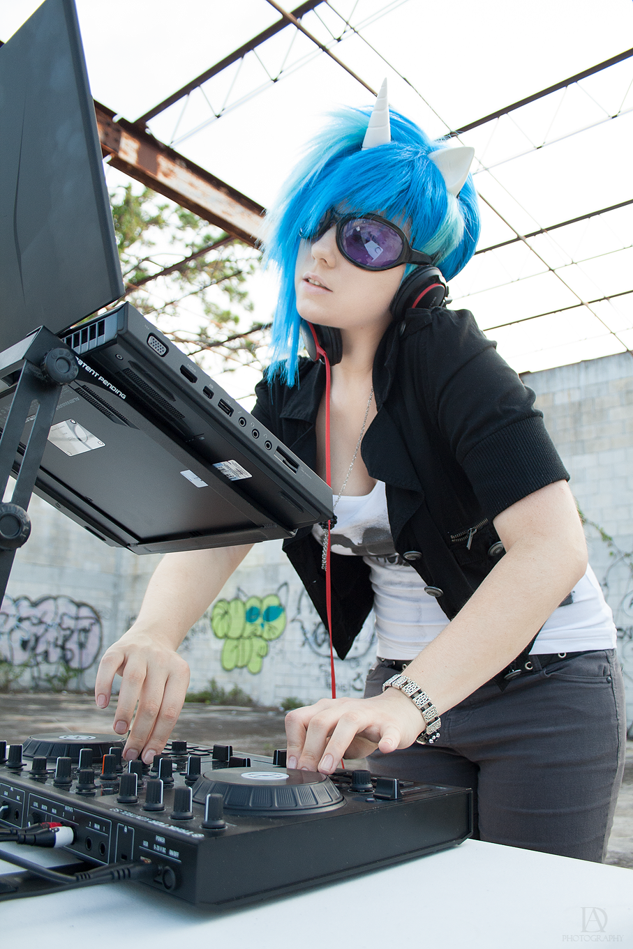 alienware bipedal black_jacket black_pants blue_hair bracelet breasts closed_legs clothing computer cosplay cute cyan_highlights dj dyed_hair environment equine eyewear female friendship_is_magic front_view goggles graffiti hair head_tilted headphones horn human jacket jeans jewelry laptop leaning leaning_forward mammal my_little_pony necklace outside photo real shirt_logo skylight solo standing studded_belt sunglasses table three-quarter_portrait three-quarter_view turntable unicorn vinyl_scratch_(mlp) white_ears white_horn white_horns white_shirt wig zipper
