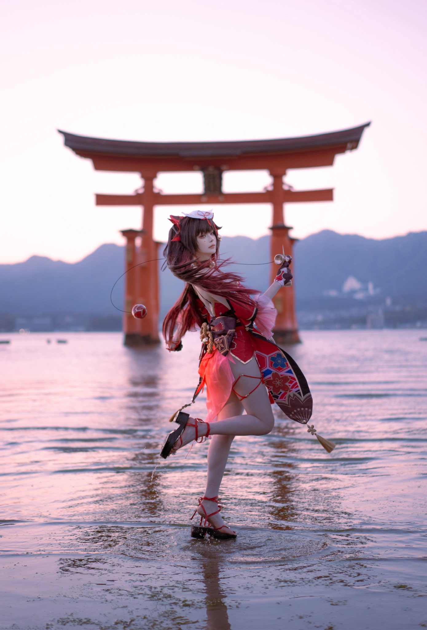 1girl blurry blurry_background brown_hair closed_mouth cosplay_photo detached_sleeves dress facial_mark floating_hair fox_mask full_body gradient_hair highres hiroshima honkai:_star_rail honkai_(series) itsukushima_shrine kendama long_hair looking_at_viewer mask mask_on_head multicolored_hair outdoors photo_(medium) red_dress red_hair sandals short_dress solo sparkle_(honkai:_star_rail) standing standing_on_one_leg thigh_strap torii twintails wading x_iaohaaaaa