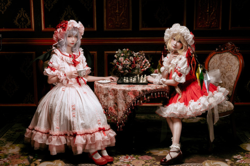 2girls ascot bat_wings blonde_hair board_game bobby_socks brooch chess chess_piece chessboard chitandaneko closed_mouth cosplay_photo crystal cup flandre_scarlet flower full_body grey_hair hat head_tilt highres holding holding_cup indoors jewelry looking_at_viewer mary_janes medium_hair mob_cap multicolored_wings multiple_girls on_chair photo_(medium) pink_headwear pink_shirt pink_skirt puffy_short_sleeves puffy_sleeves red_ascot red_brooch red_eyes red_footwear red_skirt red_vest remilia_scarlet rose saucer shiny shiny_hair shirt shoes short_sleeves sitting skirt socks table tablecloth touhou vest white_headwear white_legwear white_shirt wings wrist_cuffs