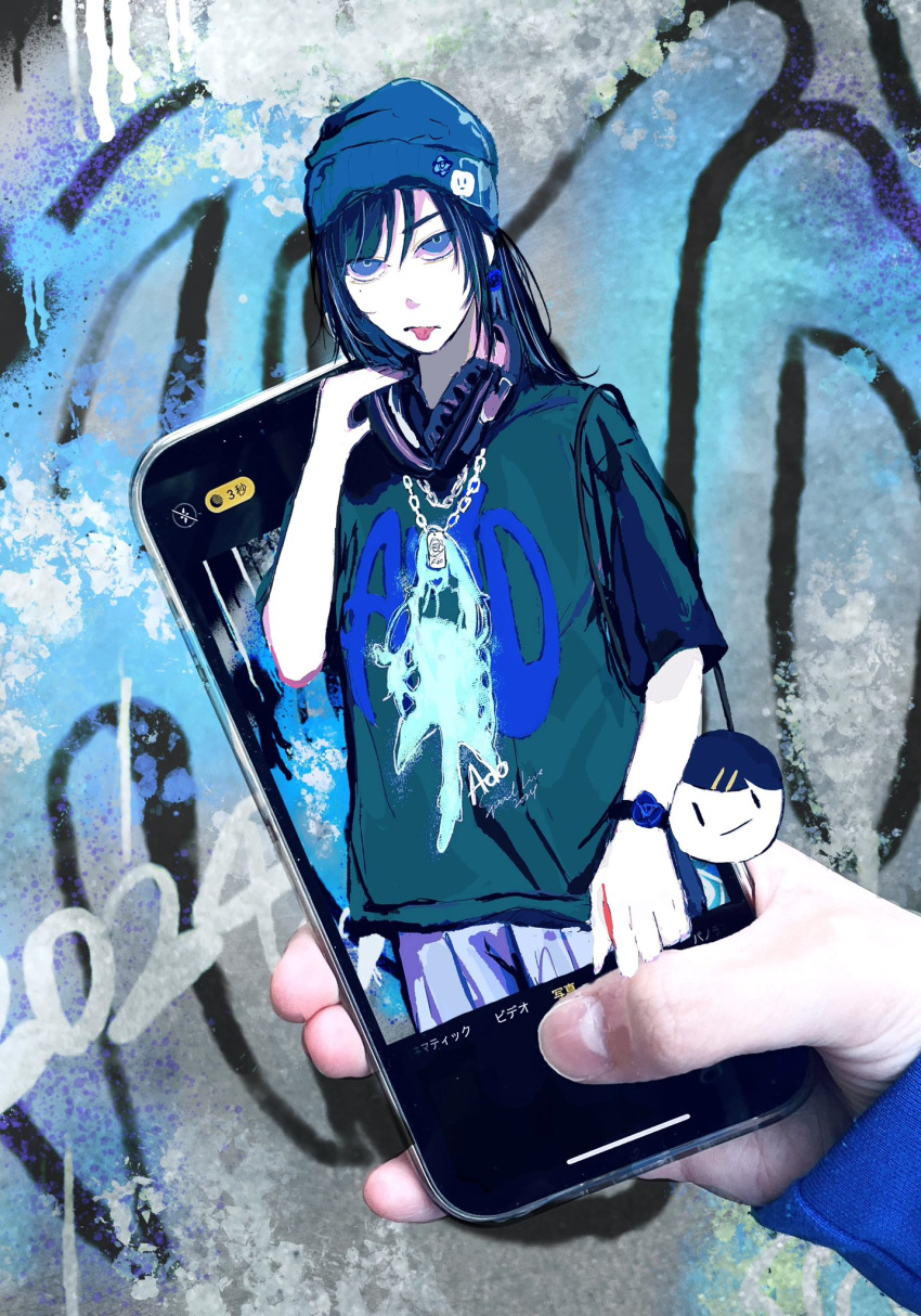 1girl ado_(utaite) black_hair blue_beanie blue_eyes blue_hair blue_shirt bracelet cellphone chando_(ado) character_name cloud_nine_inc commentary_request dog_tags graffiti hariiiiito10 headphones headphones_around_neck highres iphone jewelry looking_at_viewer multicolored_hair phone photo_background shirt short_sleeves sidelocks smartphone streaked_hair through_medium through_screen tongue tongue_out utaite