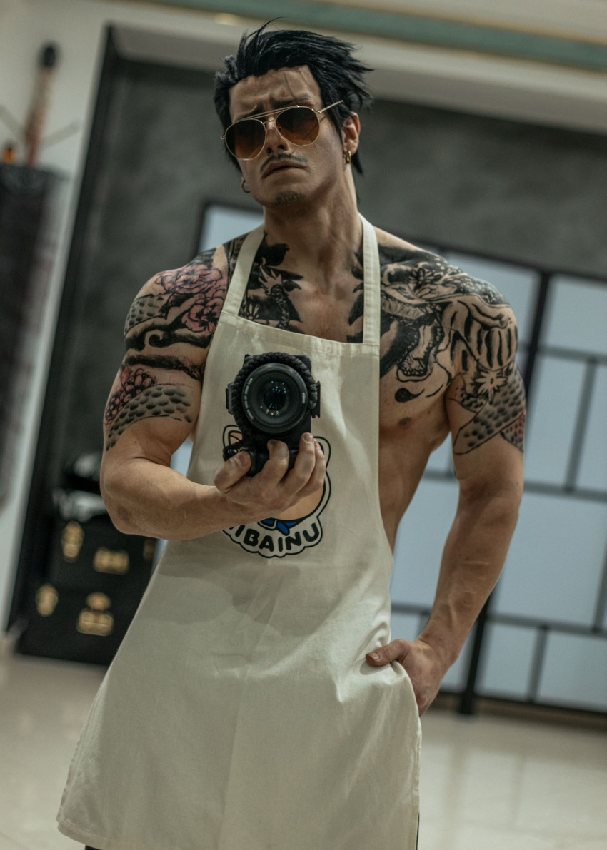 1boy apron arm_tattoo black_hair blurry blurry_background camera chest_tattoo closed_mouth cosplay_photo cowboy_shot dutch_angle earrings facial_hair gokushufudou hair_slicked_back highres holding holding_camera jewelry looking_at_viewer male_focus muscular muscular_male mustache nipple_slip nipples pectorals photo_(medium) short_hair sidepec solo sunglasses taryn_cosplay tatsu_(gokushufudou) tattoo white_apron