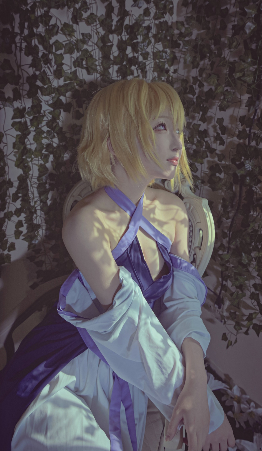 1girl absurdres bangs blonde_hair blue_eyes collarbone commentary cosplay_photo detached_sleeves dress gundam gundam_seed gundam_seed_destiny halter_dress halterneck highres hisage looking_up photo_(medium) pink_lips purple_dress purple_eyes short_hair sitting smile solo stellar_loussier