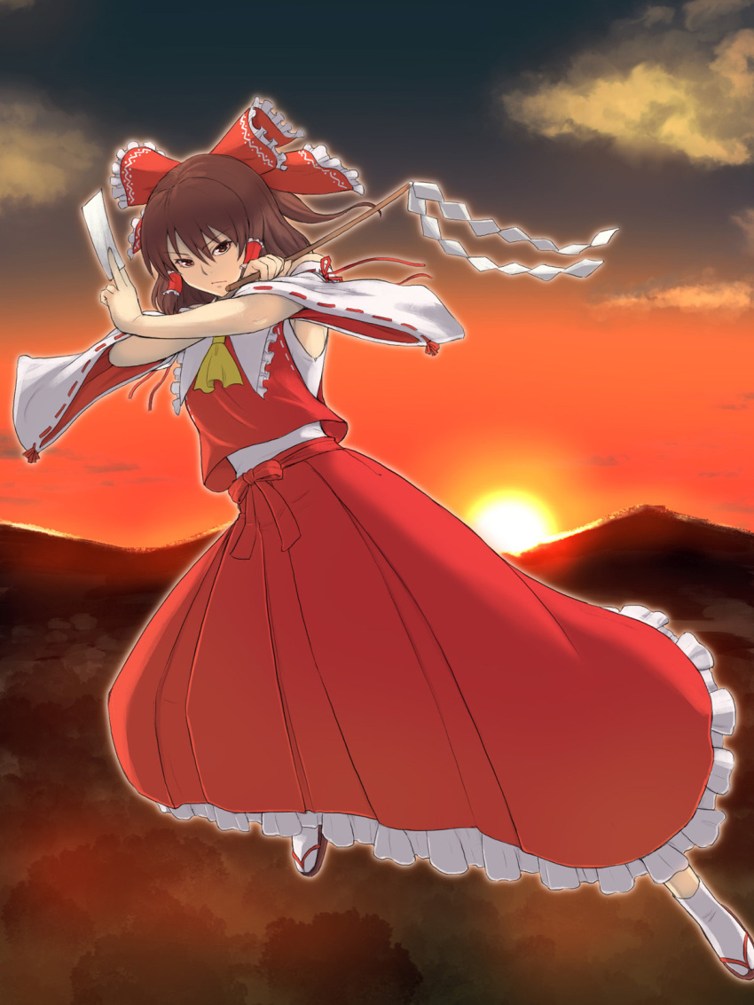 1girl ascot bow brown_eyes brown_hair closed_mouth cloud commentary detached_sleeves frilled_skirt frills full_body gohei gradient_sky hair_bow hair_tubes hakurei_reimu highres holding horizon kakone long_skirt looking_at_viewer mountainous_horizon ofuda outdoors red_bow red_shirt red_skirt ribbon-trimmed_sleeves ribbon_trim shide shirt sidelocks skirt sky socks solo sun sunset touhou white_socks wide_sleeves yellow_ascot