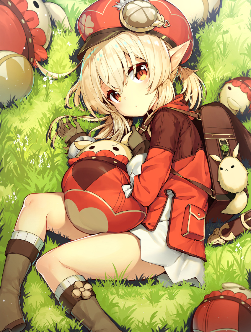 1girl :o back backpack bag bag_charm bangs blonde_hair boots brown_footwear brown_gloves charm_(object) clover darnell dress eyebrows_visible_through_hair four-leaf_clover genshin_impact gloves grass hat highres klee_(genshin_impact) knee_boots long_sleeves low_twintails lying on_side open_mouth outdoors pointy_ears red_dress red_eyes red_headwear short_twintails sidelocks solo twintails
