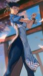  1girl absurdres black_eyes black_hair blue_dress blue_leggings bracelet breasts cherry_blossoms china_dress chinese_clothes chun-li double_bun dress hair_bun highres jewelry leggings lips looking_at_viewer medium_breasts petals shizu_(shizuillust) sky solo street_fighter street_fighter_6 stretching thighs torii 