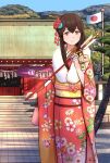  1girl akagi_(kancolle) arrow_(projectile) bag bangs breasts brown_eyes brown_hair commentary_request day floral_print hair_ornament hamaya handbag hitakikan holding japanese_clothes japanese_flag kantai_collection kimono long_hair long_sleeves looking_at_viewer obi outdoors red_kimono sash shrine smile solo tree wide_sleeves 