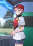  1girl apron closed_mouth cloud collared_shirt commentary_request day eyelashes grass hat highres ichiba_youichi joy_(pokemon) long_hair looking_at_viewer own_hands_together pink_eyes pink_hair poke_ball_print pokemon pokemon_(game) pokemon_sv red_headwear shirt short_sleeves shorts sky smile solo tree 