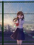  1girl bangs black_sailor_collar black_skirt black_socks breasts brown_hair chain-link_fence cityscape commentary_request crossed_bangs feet_out_of_frame fence floating_hair hair_between_eyes hair_tucking hand_up highres kusunokinawate lens_flare long_hair long_sleeves looking_at_viewer medium_skirt neckerchief original outdoors parted_lips pleated_skirt purple_eyes red_neckerchief sailor_collar school_uniform serafuku shirt skirt socks solo standing sunset white_shirt 