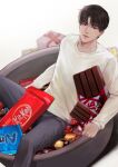  1boy absurdres black_eyes black_hair blurry candy closed_mouth depth_of_field expressionless feet_out_of_frame food gift highres in_bowl in_container kitkat looking_at_viewer male_focus minimized original ppang_sik red_ribbon ribbon short_hair sitting solo sweater white_sweater 