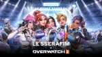  5girls arm_around_shoulder brigitte_(overwatch) brown_hair concept_art concert copyright_name cropped_jacket crowd d.va_(overwatch) fingerless_gloves gloves hat highres junkrat_(overwatch) kiriko_(overwatch) le_sserafim looking_at_viewer multiple_girls official_alternate_costume official_alternate_hairstyle official_art overwatch overwatch_2 sombra_(overwatch) stadium tracer_(overwatch) v 