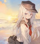  1girl anchor_symbol beach black_headwear black_sailor_collar black_serafuku black_skirt blue_eyes blush closed_mouth flat_cap grey_hair hair_between_eyes hat hibiki_(kancolle) highres its_(pixiv_61283676) kantai_collection long_hair long_sleeves neckerchief ocean pleated_skirt red_neckerchief sailor_collar school_uniform serafuku skirt smile solo 