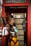  1girl ardsami bodysuit brown_hair city cosplay goggles gun leggings open_mouth outdoor overwatch phone photo short_hair smile spandex tracer_(overwatch) vest weapon 