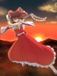  1girl ascot bow brown_eyes brown_hair closed_mouth cloud commentary detached_sleeves frilled_skirt frills full_body gohei gradient_sky hair_bow hair_tubes hakurei_reimu highres holding horizon kakone long_skirt looking_at_viewer mountainous_horizon ofuda outdoors red_bow red_shirt red_skirt ribbon-trimmed_sleeves ribbon_trim shide shirt sidelocks skirt sky socks solo sun sunset touhou white_socks wide_sleeves yellow_ascot 