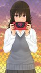  absurdres bad_id bad_pixiv_id black_hair blush brown_eyes chain-link_fence fence green_kaminari hair_between_eyes handheld_game_console heart highres holding_handheld_game_console looking_at_viewer miyamae_tooru pleated_skirt school_uniform sega_game_gear seiren skirt solo sunset sweater_vest 