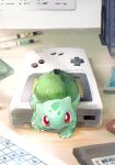  animal_focus bright_pupils bulbasaur colored_skin commentary_request fangs game_boy green_skin handheld_game_console highres indoors no_humans open_mouth plant pokemon pokemon_(creature) red_eyes smile toneko white_pupils 