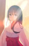  1girl backlighting bangs black_hair blurry blurry_background blush bow closed_mouth commentary_request eyebrows_visible_through_hair hakama highres hyakunin_momoko japanese_clothes kimono lens_flare long_hair looking_at_viewer miko mole mole_under_eye original purple_eyes red_bow red_hakama smile solo sunlight tareme upper_body white_kimono 