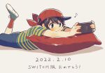  1boy baseball_cap black_eyes black_hair blue_shorts blush dated fingernails foot_up grey_background grey_footwear handheld_game_console hat holding holding_handheld_game_console looking_at_object lying male_focus mother_(game) mother_1 musical_note neckerchief ninten nintendo_switch on_stomach pillow red_headwear red_neckerchief red_socks shifumame shirt short_hair short_sleeves shorts sideways_hat socks solo striped striped_shirt translation_request 
