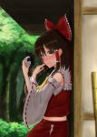  1girl absurdres against_wall arms_up bamboo_broom baozi black_hair blurry blurry_background blush broom brown_eyes commentary_request day detached_sleeves food food_on_face forest hair_ribbon hair_tubes hakurei_reimu hand_on_own_face highres hip_vent holding holding_food looking_at_viewer luke_(kyeftss) midriff nature navel outdoors red_skirt red_vest ribbon ribbon-trimmed_sleeves ribbon_trim sarashi sidelocks sideways_glance skirt solo standing sweatdrop touhou upper_body vest 