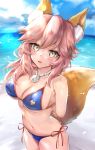  1girl absurdres animal_ear_fluff animal_ears arms_behind_back bangs bare_shoulders beach bikini blue_bikini blue_sky blush breasts cleavage collarbone fangs fate/grand_order fate_(series) fox_ears fox_girl fox_tail hair_between_eyes hane_yuki highres jewelry large_breasts long_hair looking_at_viewer navel necklace ocean open_mouth pink_hair shore sky smile swimsuit tail tamamo_(fate)_(all) tamamo_no_mae_(swimsuit_lancer)_(fate) thighs 