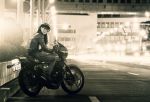  1girl bangs blurry blurry_background commentary depth_of_field gloves greyscale ground_vehicle jacket kokudou_juunigou logo long_hair long_sleeves looking_at_viewer looking_back monochrome motor_vehicle motorcycle night on_motorcycle open_mouth original outdoors pants shoes smile solo symbol_commentary 
