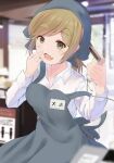  1girl apron barcode_scanner blonde_hair blurry blurry_background commentary eyebrows_visible_through_hair fang file112056 green_eyes head_scarf highres holding indoors inuyama_aoi name_tag ponytail skin_fang solo store_clerk strap_slip thick_eyebrows yurucamp 