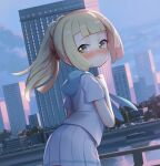  1girl bangs blonde_hair blunt_bangs blush building clenched_hand closed_mouth cloud commentary_request day fence floating_hair green_eyes hand_up lamppost leaning_forward lillie_(pokemon) long_hair looking_back outdoors pleated_skirt pokemon pokemon_(game) pokemon_sm ponytail shamonabe shiny shiny_hair shirt short_sleeves skirt sky solo water white_shirt white_skirt window 