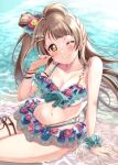  1girl absurdres bangs beach bikini bikini_skirt blush bow bracelet breasts cleavage closed_mouth commentary floating_hair frilled_bikini frills hair_bow hair_rings highres jewelry light_brown_hair long_hair looking_at_viewer love_live! love_live!_school_idol_project medium_breasts minami_kotori navel one_eye_closed ranemu scrunchie side_ponytail sitting smile solo swimsuit thigh_strap water wet wrist_scrunchie yellow_eyes 
