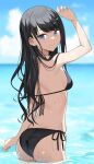  1girl arm_up asato_(fadeless) ass bangs bikini black_bikini black_hair blue_eyes blurry blurry_background breasts closed_mouth cloud commentary_request day highres horizon idolmaster idolmaster_shiny_colors kazano_hiori light_blush long_hair looking_at_viewer looking_back mole mole_under_mouth outdoors shading_eyes side-tie_bikini small_breasts smile solo standing swimsuit wading water wet 