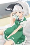  1girl 258n absurdres bangs bed black_bow black_bowtie blue_eyes blurry blurry_background blush bow bowtie breasts buttons collar collared_shirt dress eyebrows_visible_through_hair ghost_print green_dress grey_hairband hairband hand_up highres hitodama_print konpaku_youmu looking_at_viewer medium_breasts one_eye_closed open_mouth puffy_short_sleeves puffy_sleeves shirt short_hair short_sleeves silver_hair sitting solo touhou white_shirt 
