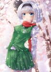  1girl bangs black_hairband blue_eyes blurry cherry_blossoms cowboy_shot depth_of_field eyebrows_visible_through_hair green_skirt green_vest hairband highres holding_own_wrist konpaku_youmu long_sleeves looking_at_viewer one_eye_closed open_mouth outdoors red_scarf reijing_etrn scarf shirt short_hair silver_hair skirt snowflakes snowing solo standing touhou tree vest white_shirt 