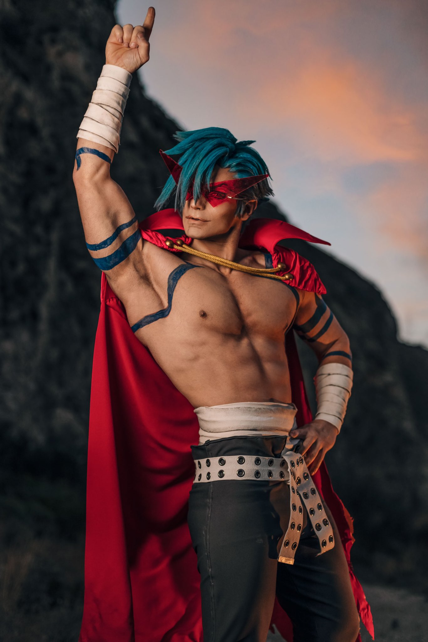 1boy abs arm_tattoo armpits bandaged_arm bandages belt black_pants blue_hair blurry blurry_background cape closed_mouth cosplay_photo cowboy_shot hand_on_own_hip hand_up highres kamina_(ttgl) looking_at_viewer male_focus mountain muscular muscular_male nipples pants pectorals photo_(medium) pointing pointing_up red-framed_eyewear red_cape short_hair sky solo taryn_cosplay tattoo tengen_toppa_gurren_lagann topless_male white_belt