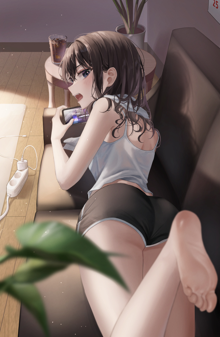 1girl absurdres angry ass bare_arms barefoot black_eyes black_shorts blurry blurry_foreground blush brown_hair camisole charger commentary_request couch day depth_of_field drink extension_cord fangs feet foot_out_of_frame foot_up glass highres holding holding_phone indoors leaf light_particles long_hair looking_at_viewer looking_back lying on_couch on_stomach open_mouth original phone plant potted_plant shadow short_shorts shorts soles solo table toes towel towel_around_neck white_camisole wolla wooden_floor