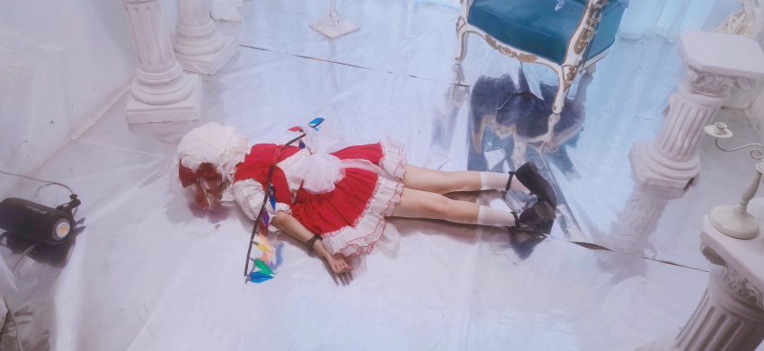 1girl back_bow black_footwear bow chair cosplay cosplay_photo flandre_scarlet flandre_scarlet_(cosplay) frilled_sleeves frills full_body hat highres indoors lying mary_janes mob_cap multicolored_wings on_floor on_stomach photo_(medium) puffy_sleeves red_skirt red_vest reflective_floor shirt shoes skirt skirt_set socks solo thighs touhou vest white_bow white_headwear white_shirt white_socks wings ysu2211
