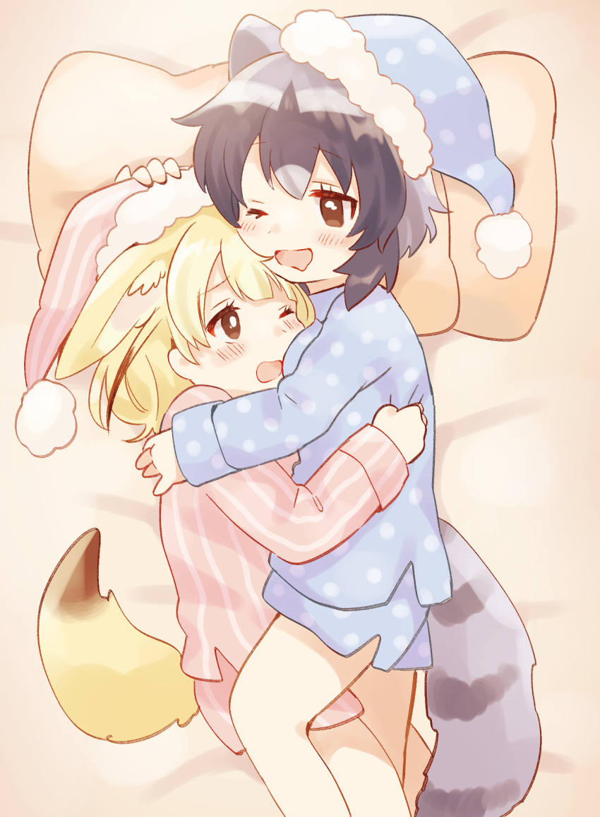 2girls animal_ears black_hair blonde_hair blue_pajamas blush brown_eyes common_raccoon_(kemono_friends) fennec_(kemono_friends) fox_ears fox_girl fox_tail hat highres hug kemono_friends multiple_girls nightcap one_eye_closed open_mouth pajamas pillow pink_pajamas raccoon_ears raccoon_girl raccoon_tail short_hair striped striped_pajamas striped_tail suicchonsuisui tail