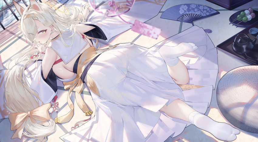 1girl animal_ears bare_shoulders blonde_hair blue_archive breasts dango detached_sleeves eyes_visible_through_hair feet food fox_ears hair_over_one_eye hand_fan highres indoors kaho_(blue_archive) large_breasts long_hair looking_at_viewer looking_back lying on_stomach sanshoku_dango sideboob socks soles solo uaxa2334 wagashi white_sleeves white_socks yellow_eyes