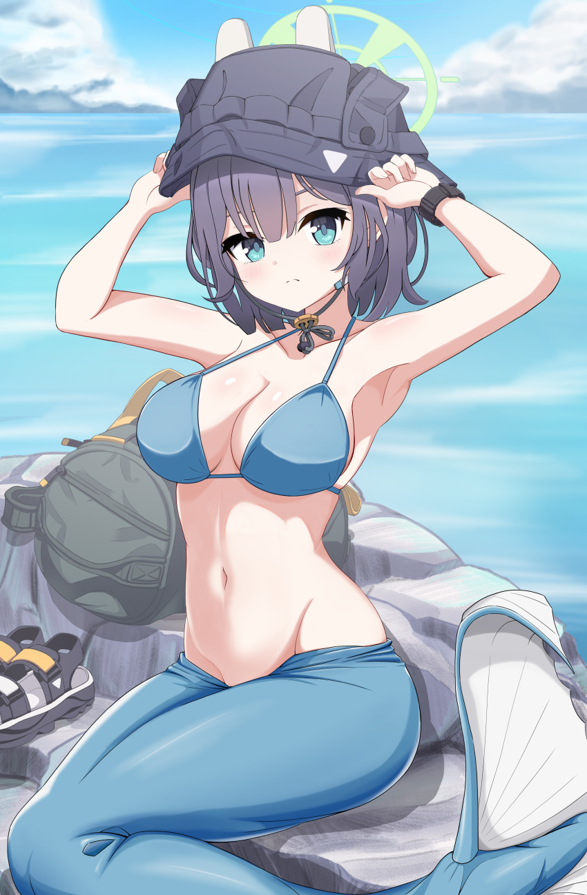 1girl absurdres arms_up backpack bag bikini black_headwear blue_archive blue_bikini blue_eyes blue_hair blush breasts bucket_hat commentary_request dark_blue_hair day halo hat highres looking_at_viewer medium_breasts medium_hair mermaid_costume monofin navel ocean official_alternate_costume outdoors poorunii rock saki_(blue_archive) saki_(swimsuit)_(blue_archive) sitting solo stomach swimsuit variant_set watch wristwatch
