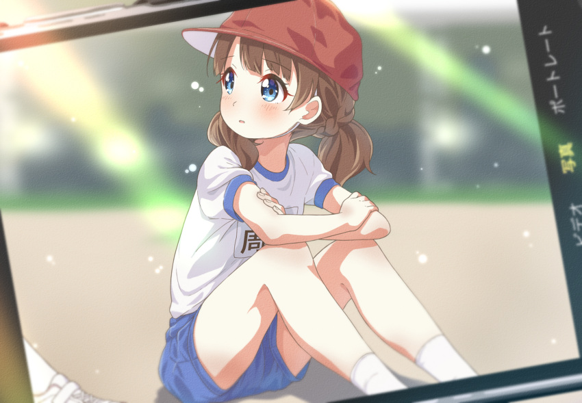 1girl arm_rest blue_eyes blue_shorts blurry blurry_background blush brown_hair cellphone commentary day eyelashes flat_chest hat highres idolmaster idolmaster_million_live! legs looking_at_another medium_hair name_tag on_floor outdoors parted_lips phone photo_(object) red_headwear shirt short_sleeves short_twintails shorts sitting smartphone socks solo suou_momoko thighs toma_(shinozaki) twintails white_shirt white_socks