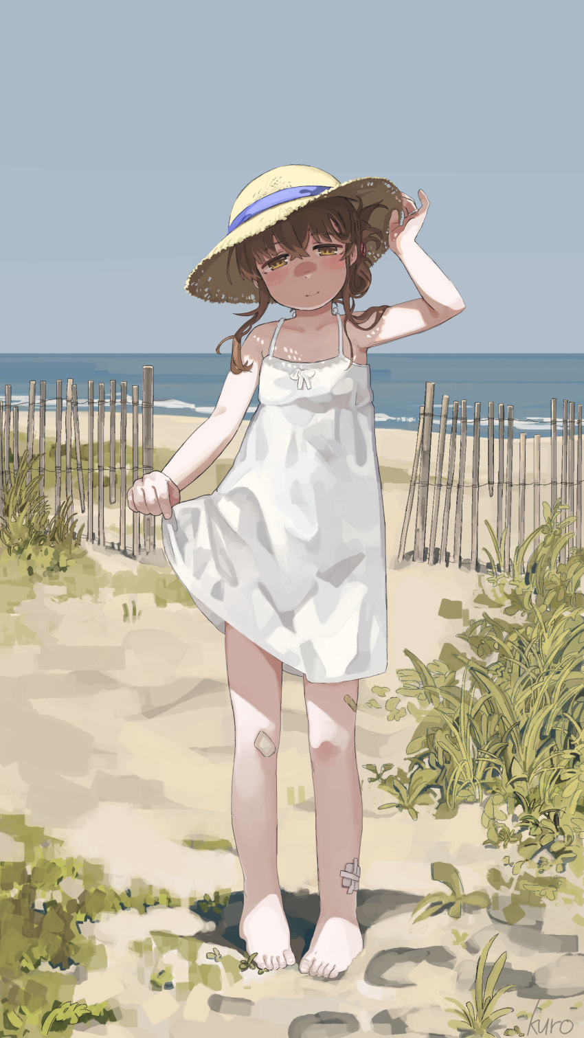 1girl absurdres artist_name bamboo_fence bandaid bandaid_on_knee bandaid_on_leg barefoot blue_ribbon blush brown_eyes clear_sky closed_mouth day dress fence folded_ponytail full_body grass hair_bun hand_on_headwear hat hat_ribbon head_tilt highres horizon inazuma_(kancolle) kantai_collection kuro4221 looking_at_viewer ocean pigeon-toed ribbon shaded_face shore skirt_hold sky smile solo spaghetti_strap standing straw_hat sun_hat sundress tareme white_dress