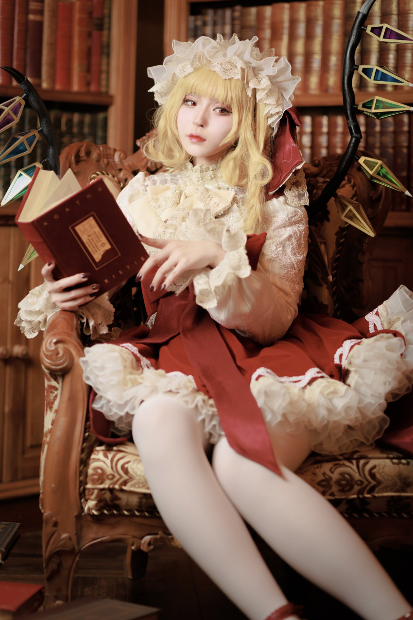 1girl absurdres adapted_costume black_nails blonde_hair book bookshelf closed_mouth cosplay_photo feet_out_of_frame flandre_scarlet hat highres holding holding_book indoors koiyume615 library long_sleeves medium_hair mob_cap multicolored_wings nail_polish on_chair open_book pantyhose petticoat photo_(medium) red_eyes red_skirt red_vest shirt sitting skirt solo touhou vest white_hat white_pantyhose white_shirt wings wooden_chair wooden_floor