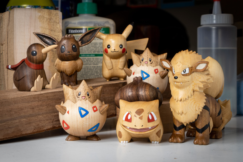 :3 :d absurdres arcanine bird bulbasaur commentary creature eevee english_commentary fangs gen_1_pokemon gen_2_pokemon happy highres kiwi looking_at_viewer no_humans open_mouth photo pikachu pokemon pokemon_(creature) sculpture sean_syman sitting smile standing togepi wood