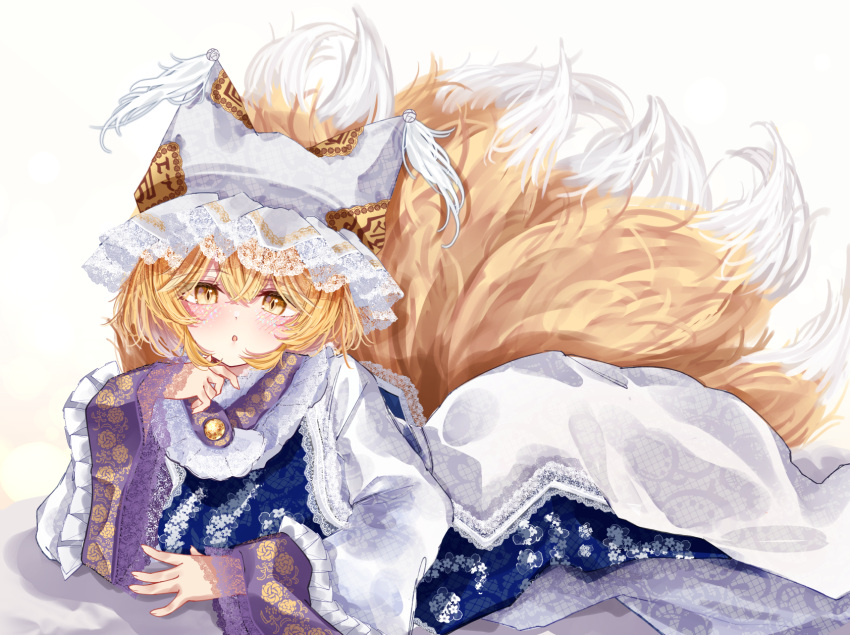 1girl :o animal_ears animal_hat blonde_hair blue_tabard commentary_request dress feet_out_of_frame fox_girl fox_tail frilled_sleeves frills hand_up hat highres lace-trimmed_headwear lace-trimmed_sleeves lace_trim long_sleeves looking_at_viewer lying mob_cap multiple_tails on_ground on_stomach open_mouth sarasadou_dan short_hair solo tabard tail touhou white_dress white_headwear wide_sleeves yakumo_ran yellow_eyes