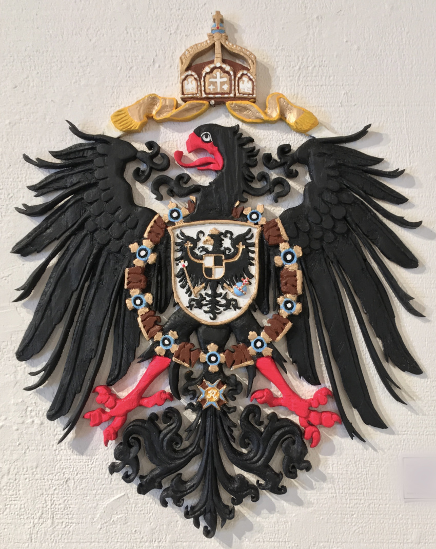 2019 accipitrid accipitriform avian beak bird black_body black_feathers carving christian_cross christian_symbol christianity cross crown crucifix eagle feathered_wings feathers feral german german_empire germany hi_res jewelry markhor_(artist) necklace painted photo red_beak red_feet regalia religion ribbons shield solo tail_feathers wings wood yellow_beak yellow_feet