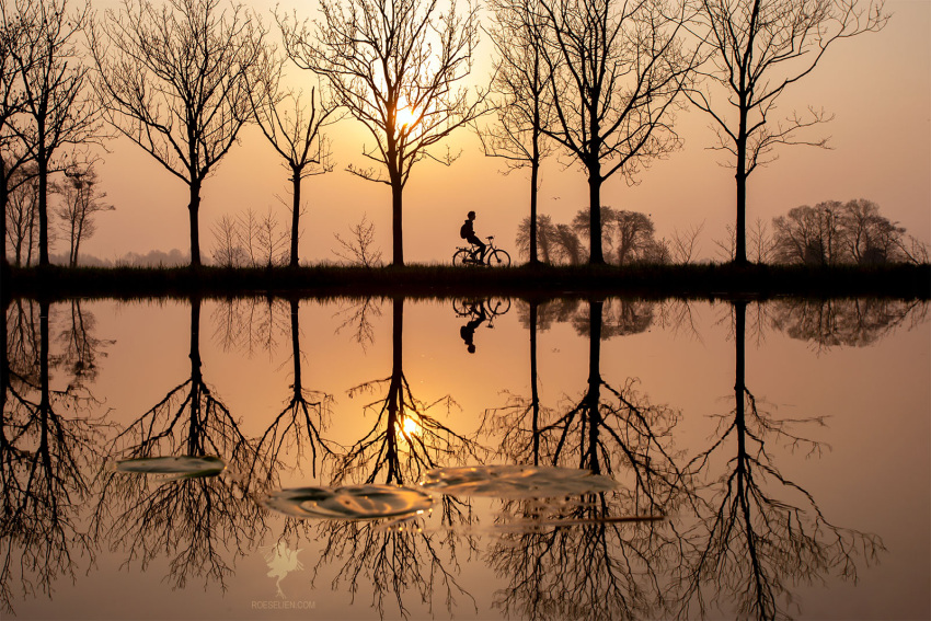 artist_request bicycle biker child commentary_request english_commentary ground_vehicle highres lake lightning original outdoors reflection scenery serenity silhouette sunrise sunset water