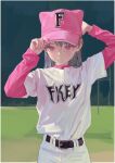  1girl artist_name baseball_cap baseball_uniform belt brown_hair clothes_writing expressionless fkey hair_behind_ear hat highres layered_sleeves long_hair long_sleeves looking_ahead original outdoors pants pink_eyes pink_headwear shirt short_over_long_sleeves short_sleeves solo sportswear 