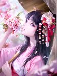  1girl absurdres bangs black_eyes black_hair blurry blurry_background blurry_foreground branch cherry_blossoms day hair_ornament hair_over_shoulder hand_up highres holding holding_umbrella kanzashi lizchief long_hair mouth_hold nose original petals second-party_source signature solo umbrella upper_body wind 