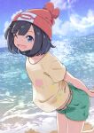  1girl ;d absurdres arms_behind_back beach beanie black_hair blue_eyes blue_sky cloud day floral_print foot_up from_side green_shorts hat highres leaning_forward looking_at_viewer negimiso1989 ocean one_eye_closed open_mouth outdoors own_hands_together pokemon pokemon_(game) pokemon_sm red_headwear selene_(pokemon) shirt short_hair short_shorts shorts sky smile solo standing standing_on_one_leg t-shirt water yellow_belt yellow_shirt 