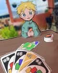  1boy bicycle blonde_hair blue_eyes blue_shirt blurry blurry_background blush_stickers butters_stotch card child depth_of_field highres holding holding_card looking_at_viewer omochisan216 open_mouth outdoors outline playing_card pov shirt smile solo south_park table turtleneck uno_(game) white_outline 