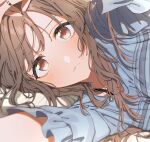  1girl blue_shirt blush bra_strap brown_eyes brown_hair eyes_visible_through_hair hand_on_own_head highres idolmaster idolmaster_shiny_colors iwawa jewelry long_hair looking_at_viewer lying pendant shirt solo tsukioka_kogane 