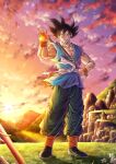  1boy absurdres black_hair closed_eyes dougi dragon_ball dragon_ball_(object) dragon_ball_z facing_viewer full_body grin highres holding male_focus mocky_art mountain muscular muscular_male pants sash sky smile solo son_goku standing sunset white_sash wristband 