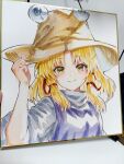  1girl blonde_hair brown_hat chinese_commentary closed_mouth commentary_request hair_ribbon hat highres l0e9s29p long_sleeves looking_at_viewer moriya_suwako photo_(medium) purple_vest red_ribbon ribbon shikishi smile solo touhou traditional_media tress_ribbon upper_body vest wide_sleeves yellow_eyes 